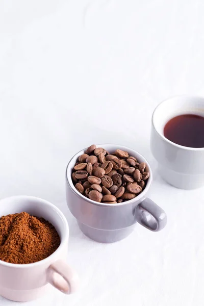 Tre koppar kaffe i olika skick - bönor, nymald och kaffedrycker på en ljusgrå bakgrund i marmor. — Stockfoto