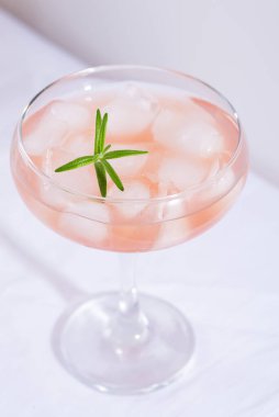 Masadaki beyaz masa örtüsünün üzerinde biberiyeli ve buzlu pembe kokteyl.
