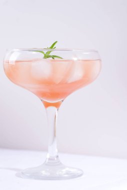 Masadaki beyaz masa örtüsünün üzerinde biberiyeli ve buzlu pembe kokteyl.