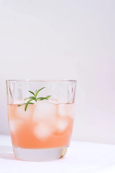 Cóctel rosa con romero y hielo en vaso sobre un mantel blanco sobre la mesa —  Fotos de Stock