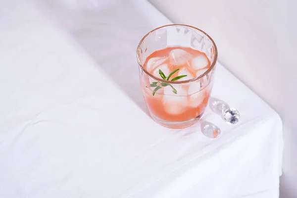 Cóctel rosa con romero y hielo en vaso sobre un mantel blanco sobre la mesa —  Fotos de Stock