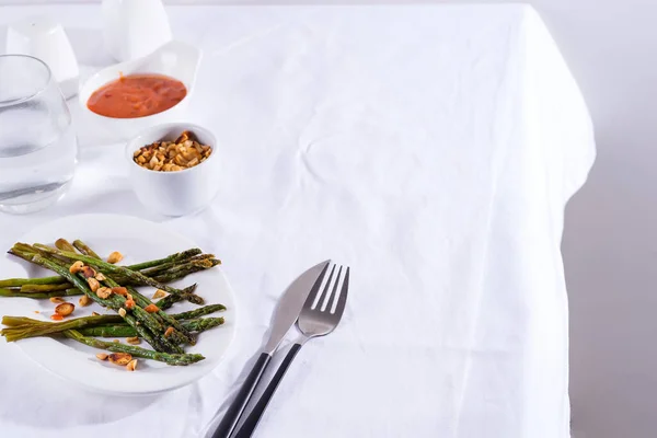 Asparagus roasted in olive oil with crushed walnuts and sauce on a white plate. Vegetarian food. — Stock Photo, Image