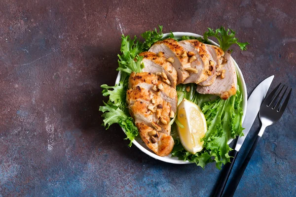 Izgara tavuk göğsü, taze friz salatası ve limonla birlikte koyu taş arka planda bir tabakta. — Stok fotoğraf