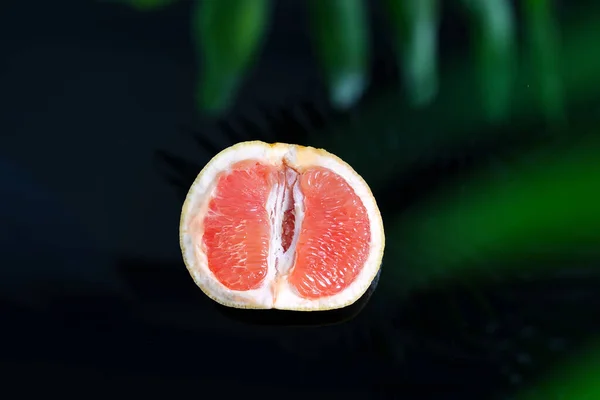 Half of fresh ripe grapefruit against a blurred natural background with green palm leaf. — Stock Photo, Image
