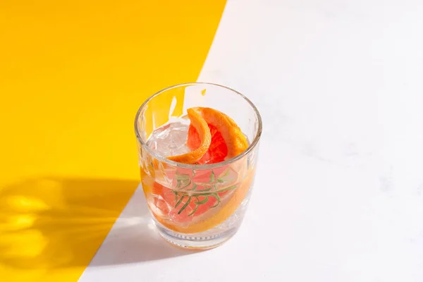 Refreshing cold summer drink in a glass with slice of grapefruit and ice cubes on a duotone yellow white background. — Stock Photo, Image