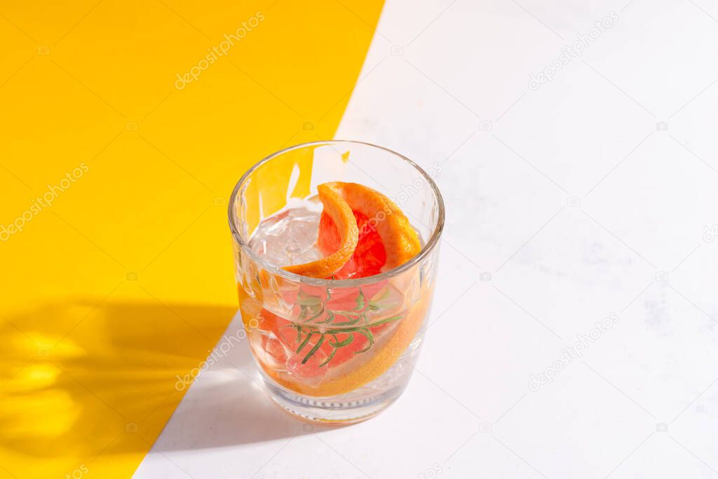 Refreshing cold summer drink in a glass with slice of grapefruit and ice cubes on a duotone yellow white background.