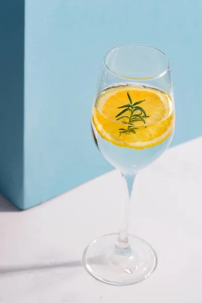 Cóctel frío casero de verano en un vaso con rodaja de limón en una mesa blanca con sombra contra la pared azul pastel . —  Fotos de Stock