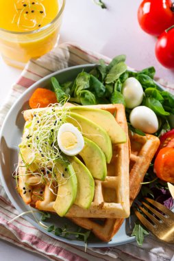 Kahvaltı vakti geldi. Kahvaltı için salatalı waffle, yumurta, meyve suyu ve avokado. Yukarıdan görüntüle.