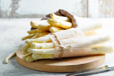 Taze toplanmış çiğ organik beyaz kuşkonmaz paketleri açık gri bir arka planda tahta bir tahtada.