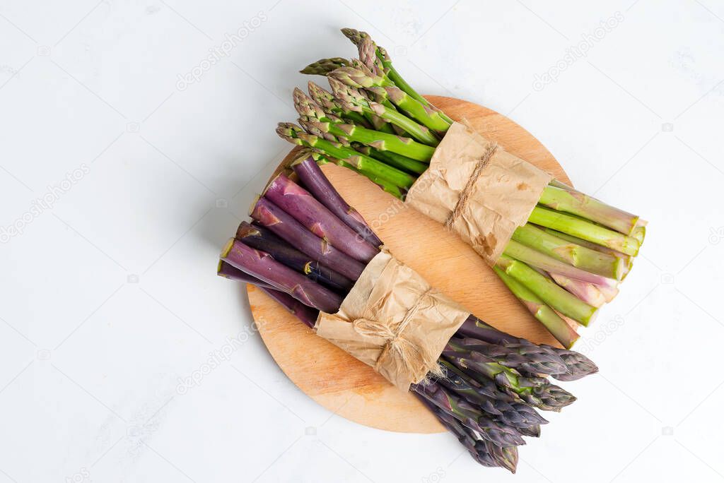 Two bundles of fresh natural organic green and purple asparagus vegetables on a wooden board and marble background.