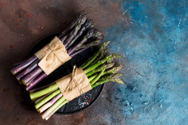 Taze, organik, iki paket yeşil ve mor kuşkonmaz. Koyu taştan bir arka planda..