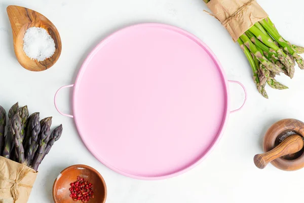 Draufsicht auf Koch Hintergrund mit Sträußen von frischem natürlichen Bio-Spargelgemüse mit verschiedenen Gewürzen und rosa Teller. — Stockfoto