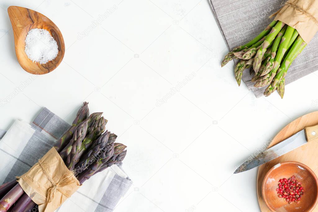 Food backdrop with bundles of fresh natural green and purple asparagus vegetables and different species on a marble background.