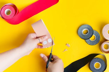 Farklı renklerde bantlanmış özel fizyoterapi ve kadın elleri sarı arka planda bej bant kesmeye başlıyor..