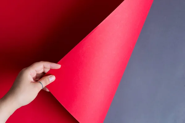 La mano de la mujer gira la hoja de papel roja sobre un fondo negro con sombras suaves . — Foto de Stock