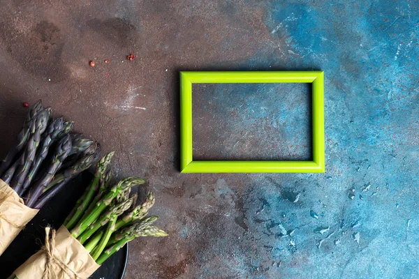 Kreative Komposition aus Fotorahmen und frischen natürlichen Bio-Spargelsträußen auf dunklem Steinhintergrund. — Stockfoto