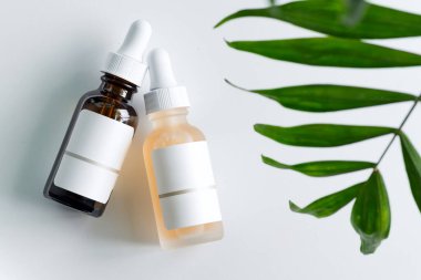 İki şişe doğal losyonlu kozmetik el yapımı seti ya da açık gri arka planda tropikal yapraklı gerekli yağ.