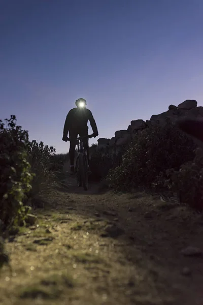 Ciclista desciende la colina por la noche iluminado por la linterna — Foto de Stock