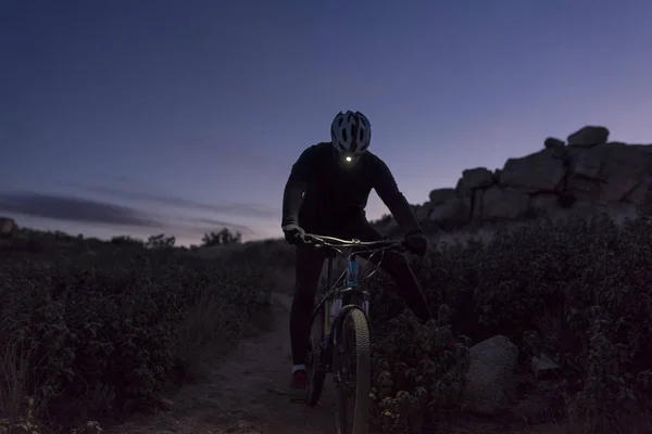 Ciclista desciende la colina por la noche iluminado por la linterna — Foto de Stock