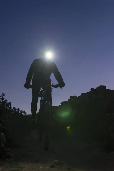 Ciclista desciende la colina por la noche iluminado por la linterna — Foto de Stock