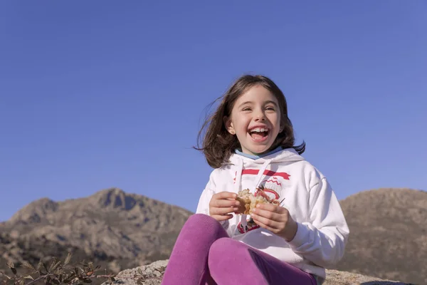 Menina sorridente restaura a força com um sanduíche na montanha — Fotografia de Stock