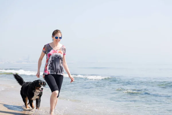 Happy woman playing with dog on beach — Stock Photo, Image