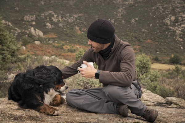 Młody człowiek siedzi na szczycie góry z psem i kubek — Zdjęcie stockowe