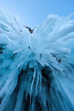Mağara kemerlerinden sarkan mavi uzun buz saçakları. Kış sarkıtları. Mavi gökyüzündeki uzayı kopyala. Dikey yönelim.