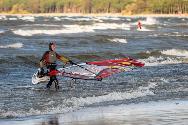 Tallinn, Estland - 18 oktober 2008: En vindsurfare i kostym bär en segelbräda ur havet. — Stockfoto