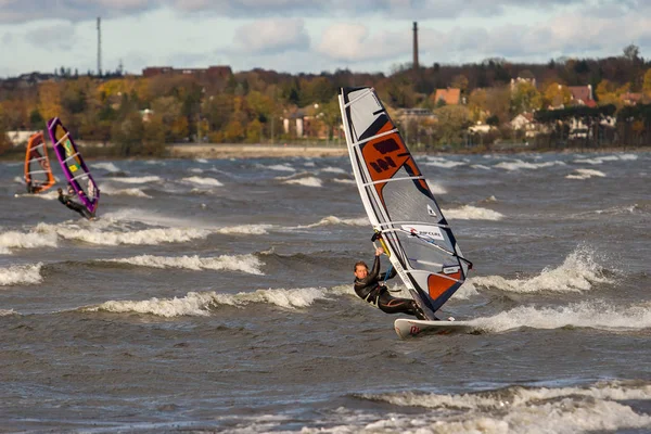 Tallinn, Estland - 18 oktober 2008: En vindsurfare i kostym rullar längs vågorna på en bräda med segel med stark lutning i blåsigt väder. — Stockfoto