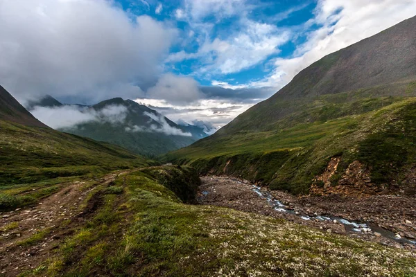 Topraktaki ırmak ve etrafındaki dağlar tarafından oluşturulan bir yarık. Dağlık kayalık patika. Bulutlu mavi gökyüzü. Yatay.