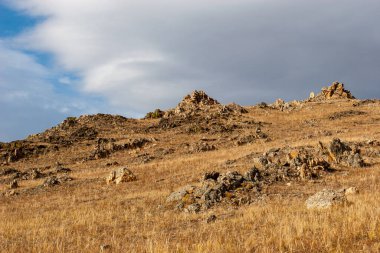 Tepede taşlar ve gökyüzünde bir bulut var. Sarı çimenler. Büyük taşlar..