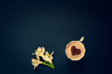 Minimalist düz yatış. Birkaç tomurcuk çiçek ve krema ve tarçınlı kahve koyu mavi arka planda bir kupa içinde kalp şeklinde. Sarı yapraklı beyaz. Gözetleme. Üzerine boşluk kopyala.