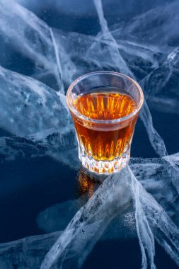 Baykal Gölü 'nün şeffaf buzunun üzerinde küçük bir bardaktaki viski duruyor. Buzdaki derin ve güzel çatlaklar. Bir bardak alkole odaklan. Dikey.