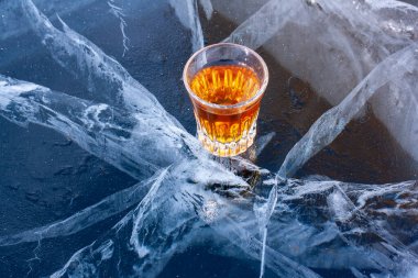 Gölün çatlamış buzunda bir bardak viski var. Soğuk viski. Güzel derin beyaz çatlakları olan mavi buz. Yan taraftan üstten bak. Alkol reklamı. Yatay.