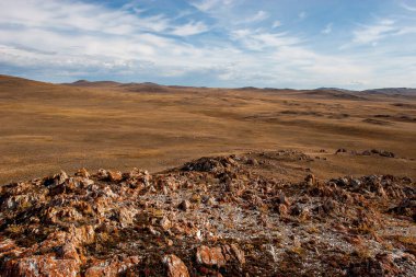 Bozkırda kırmızı yosun olan taşlar. Gökyüzünde bulutlar var. Güneşli.