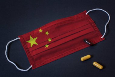 Solunum hastalıklarına, virüslere ve kapsül haplarına karşı korunmak için Çin bayrağı gibi boyanmış tıbbi yüz maskesi. Koruyucu sargı bezi. Karanlık arka plan. Yatay.