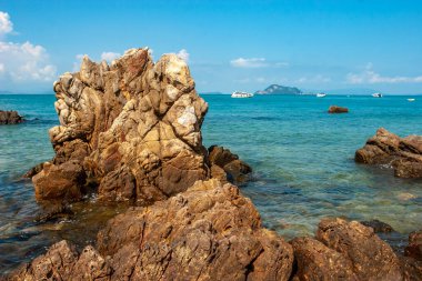 Turkuaz denizden sarkan güzel kayalar. Uzakta bir sürü tekne var. Hava güneşli. Bulutlu mavi gökyüzü. Yatay.