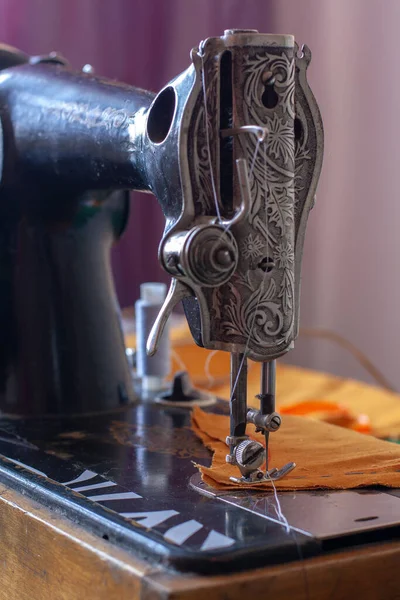 Old retro sewing machine and orange fabric ready for sewing. The presser foot is lowered. Shallow depth of field. Focus on the presser foot. Vertical.