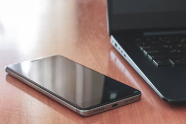 İş konsepti cep telefonu ve siyah dizüstü bilgisayar masada. Seçici sığ bir şekilde telefona odaklan. Parlak arka plan ışığı. Yatay.