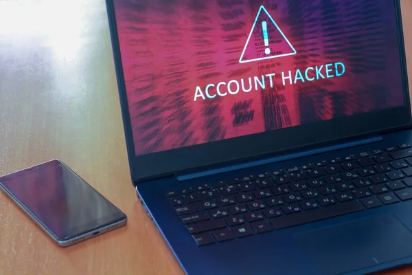 Bilgisayar ekranında hacklenmiş hesap konsepti ve karanlık ekranlı bir masada cep telefonu. Ünlem sembollü üçgen uyarı işareti. Kırmızı soyut arka plan. Yatay.