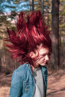 Saçını arkaya atmayı kes. Kızıl saçlı genç kız üst katta durmuş. Bulanık saçlar hareket halinde. Kum ceketi ve kazak. Ağaçlarla bulanık bir arkaplan. Dikey.