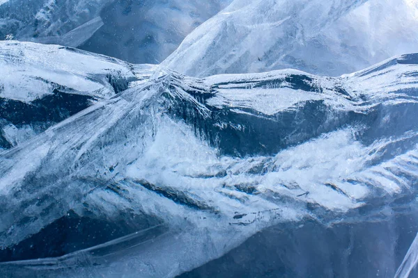 Interesting cracks in the thick ice of the lake are similar to mountain ranges. Thick blue transparent ice. Horizontal.