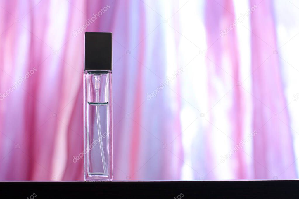 A long perfume bottle stands on a bright pink background with overexposure. Glass vial with a dark metal cap. Blank for mock up. Copy space. Blurred background. Horizontal.