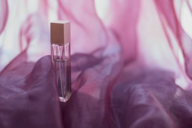 Pembe havadar kumaşlı uzun bir parfüm şişesi. Yüzü cam şişe. Dalgalı hafif kumaş. Model için boş. Uzayı kopyala Yatay.