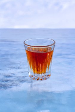 Mavi buzun üzerinde bir bardak viski duruyor. Soğuk viski. Yan taraftan üstten bak. Alkol reklamları için. Arka plan bulanık. Dikey.