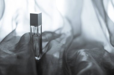 Havadar kumaşın üzerine renkli parfüm sürülmüş uzatılmış bir şişe. Yüzü cam şişe. Dalgalı hafif kumaş. Model için boş. Uzayı kopyala Yatay.