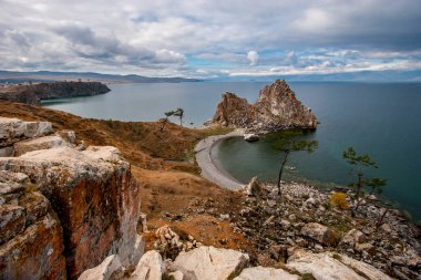 The sacred rock Shaman on the island of Olkhon on Lake Baikal. Big stones in the foreground. The sky is cloudy. The water in the lake is calm. Top view. Horizontal. clipart