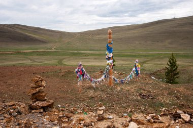 Tepelerin arka planında şaman ayinleri için kurdeleli kutsal sütunlar. Buryatia 'nın şaman ayini. Yakınlarda bir Cairn var. Yatay.