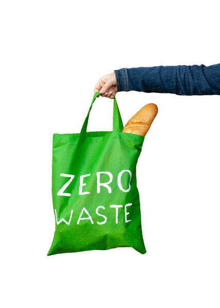 Green eco bag with a white text zero waste in the hand isolated on white background. French bread is visible in the bag. Vertical.